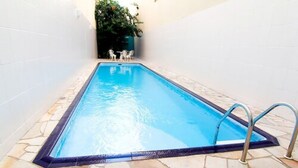 A rectangular swimming pool with a stone tile border and a metal ladder on one side. - Itajai Express (Itajai)