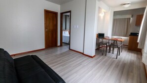 A modern living room with a black sofa, a dining area with a wooden table and chairs, and a kitchen area with cabinets and a countertop. - Itajai Express (Itajai)