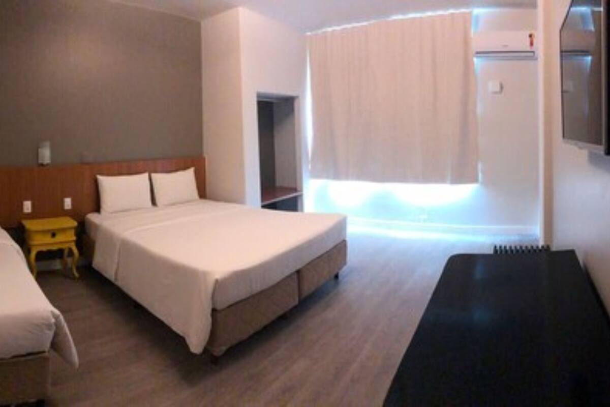 A hotel room with two single beds, a small table, and a large bed.
