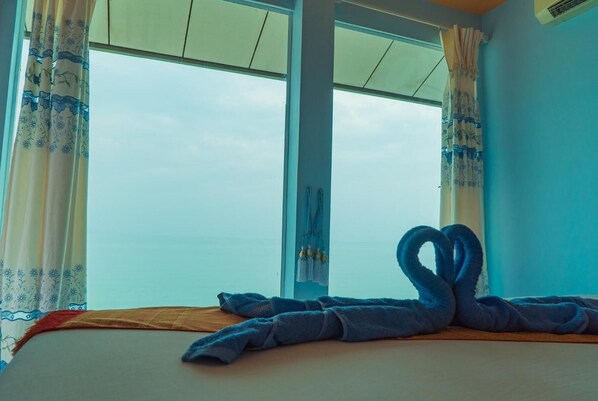A room with a bed, two windows with curtains, and a towel artfully arranged on the bed.