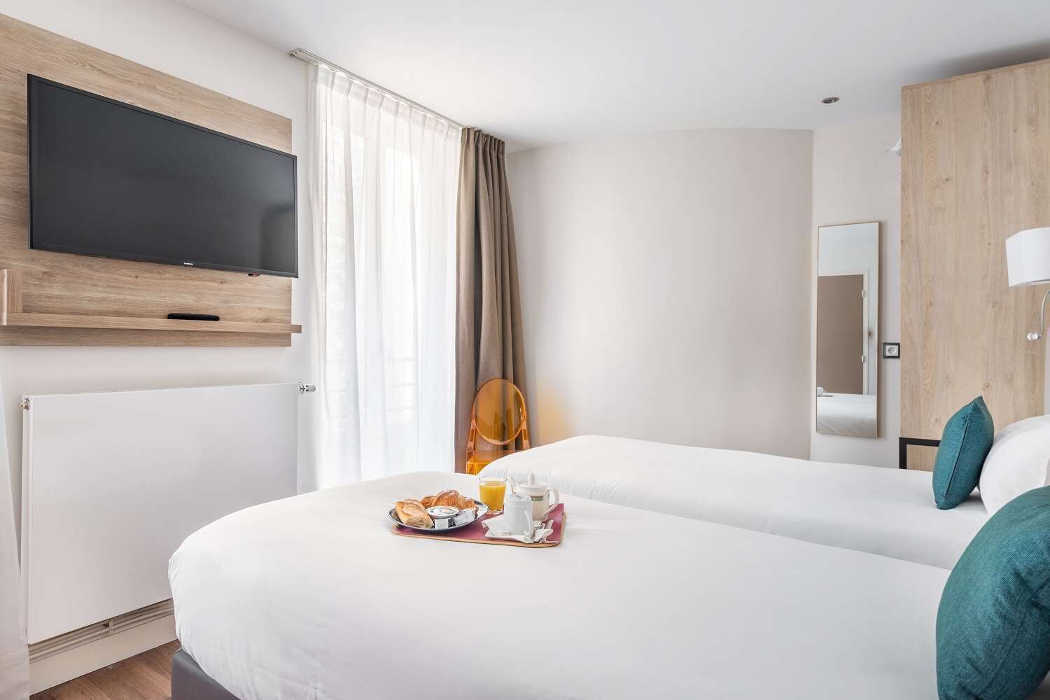 Ein Hotelzimmer mit zwei Betten, einem Flachbildfernseher, einem Frühstückswagen und einem Spiegel.