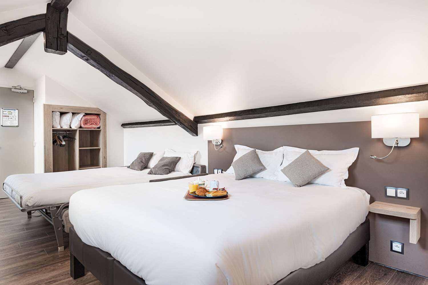 Une chambre d’hôtel avec deux lits, une armoire en bois, une table de chevet avec une lampe et un plateau contenant des articles pour le petit-déjeuner.