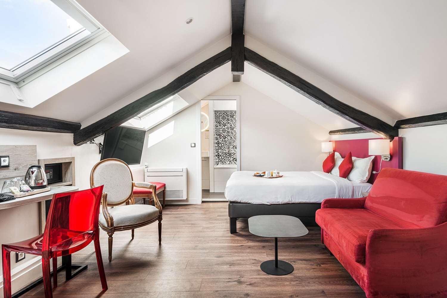 A cozy attic bedroom with a bed, red furniture, a desk with a chair, and a skylight.