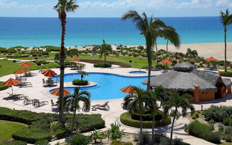 A resort with a large pool, palm trees, and a beach view.