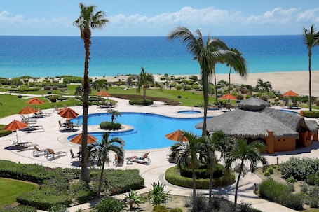 A resort with a large pool, palm trees, and a beach view.