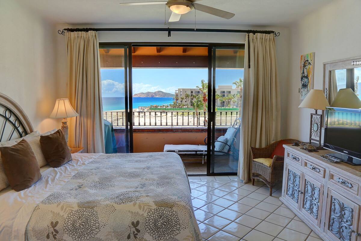 Quarto de hotel com cama, televisão, varanda vista para o mar e área de refeições.