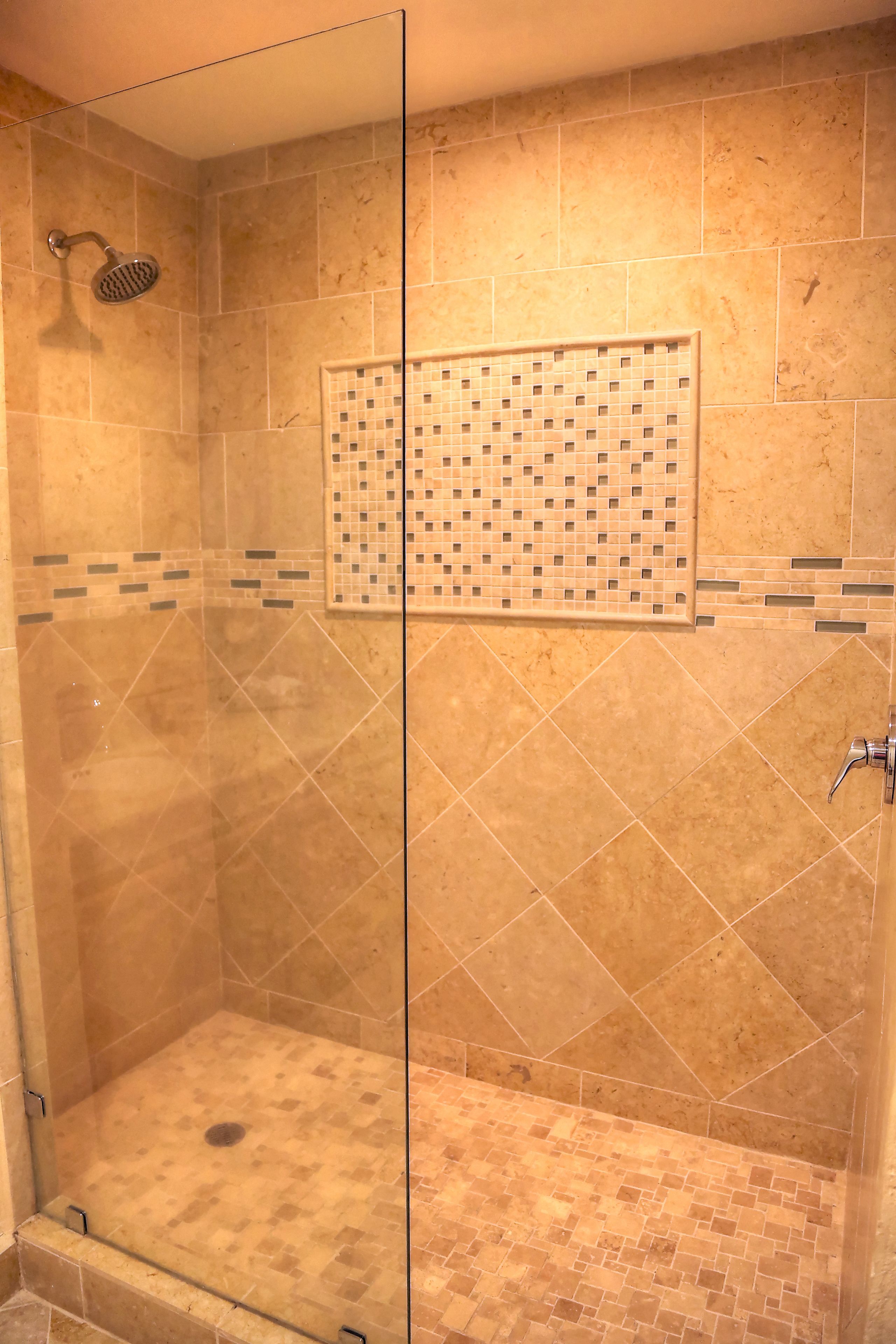 Una ducha con mampara de vidrio, piso y paredes de azulejos, un cabezal de ducha y un panel de control.
