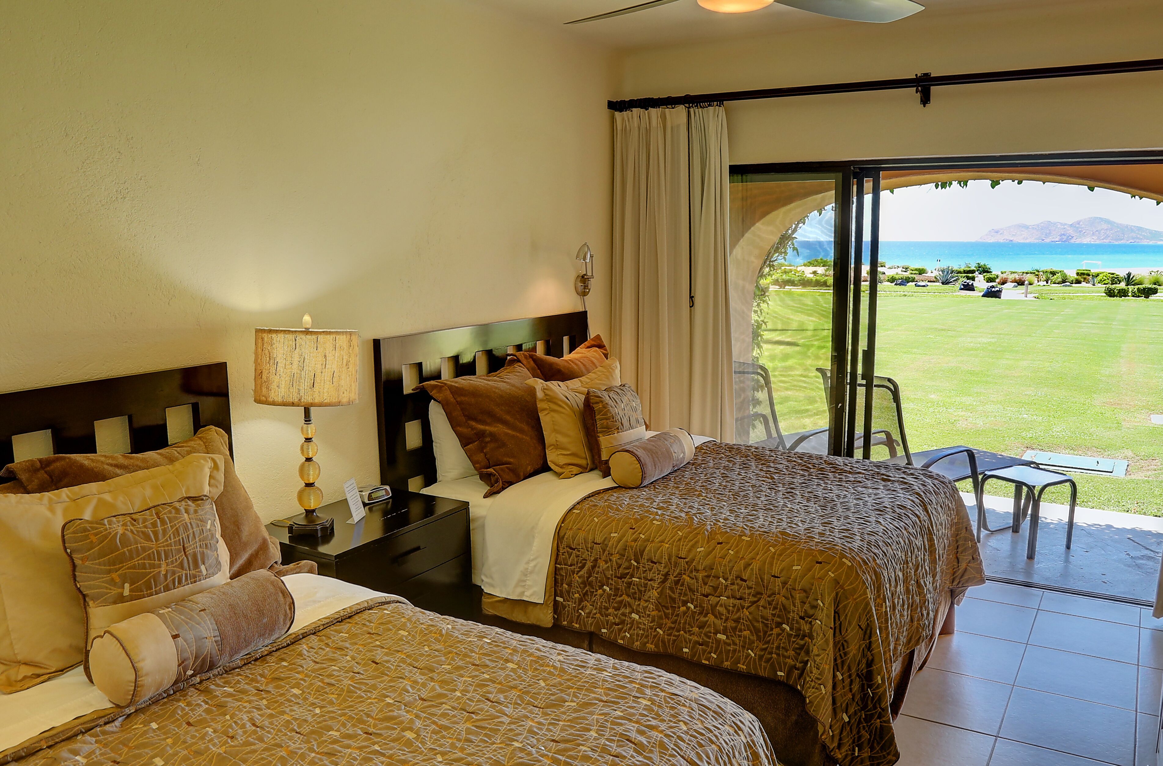 Habitación de hotel con dos camas, una mesita de noche, una lámpara y vistas a un campo de golf y montañas.