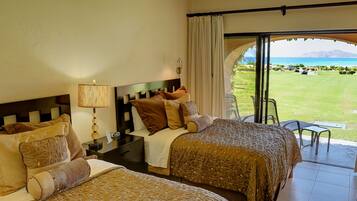 Habitación de hotel con dos camas, una mesita de noche, una lámpara y vistas a un campo de golf y montañas.