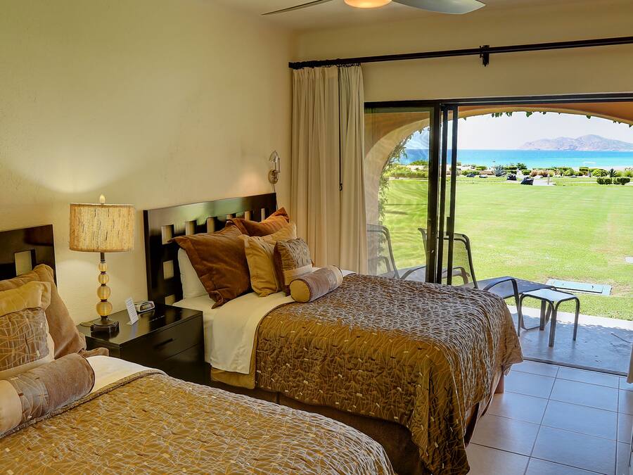 Habitación de hotel con dos camas, una mesita de noche, una lámpara y vistas a un campo de golf y montañas.
