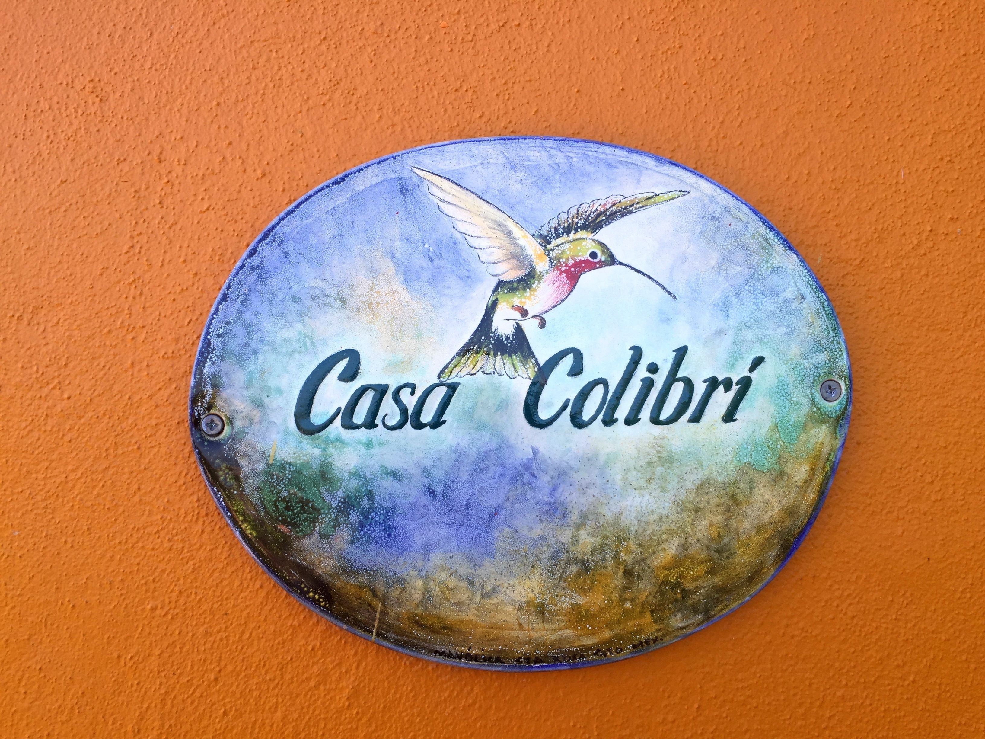 Un panneau circulaire représentant un colibri et portant l’inscription « Casa Colibri », le tout sur un mur orange.