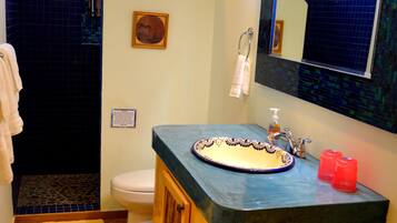A bathroom with a blue-tiled shower, a white toilet, a wooden vanity with a sink, and a mirror above the sink.