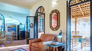 Amplia sala de estar con un sofá de cuero, una mesa de comedor con sillas, un espejo grande y vistas a un patio exterior a través de una puerta abierta.