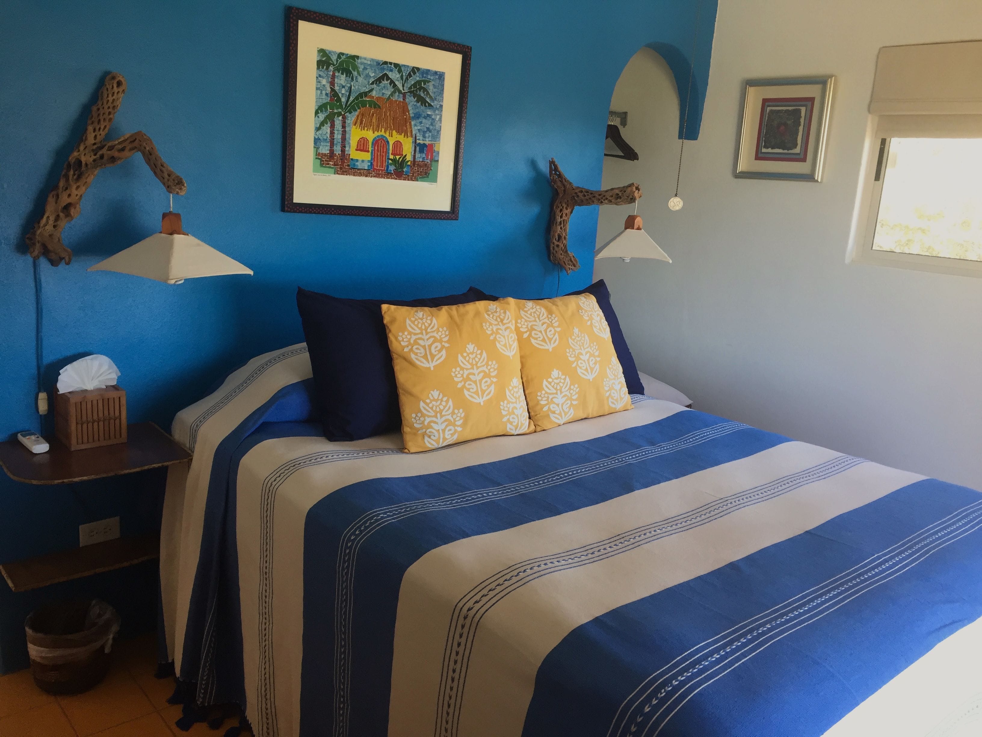 Une chambre à coucher avec un lit, une table de chevet, une lampe, un tableau au mur et une fenêtre.