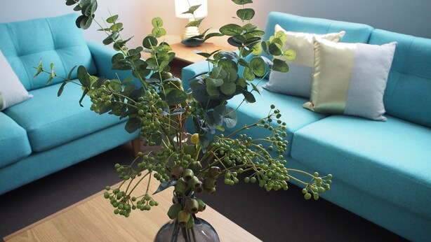 A living room with a blue sofa, a wooden coffee table, and a vase with green plants. - City Quarters on Brewer (Perth)