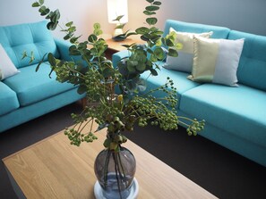 A living room with a blue sofa, a wooden coffee table, and a vase with green plants. - City Quarters on Brewer (Perth)