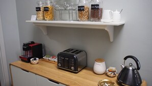 A kitchen counter with a coffee maker, toaster, kettle, and jars of coffee and cereal. - City Quarters on Brewer (Perth)