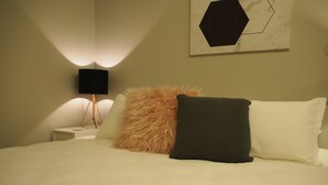 A neatly made bed with a fluffy pillow and a dark pillow, a bedside lamp, and a wall-mounted artwork. - City Quarters on Brewer (Perth)