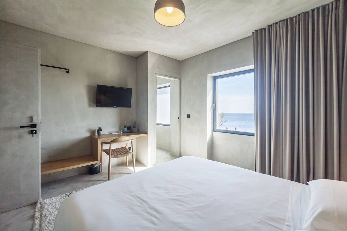 A modern hotel room with a large bed, a desk with a chair, a television, and a window with curtains.