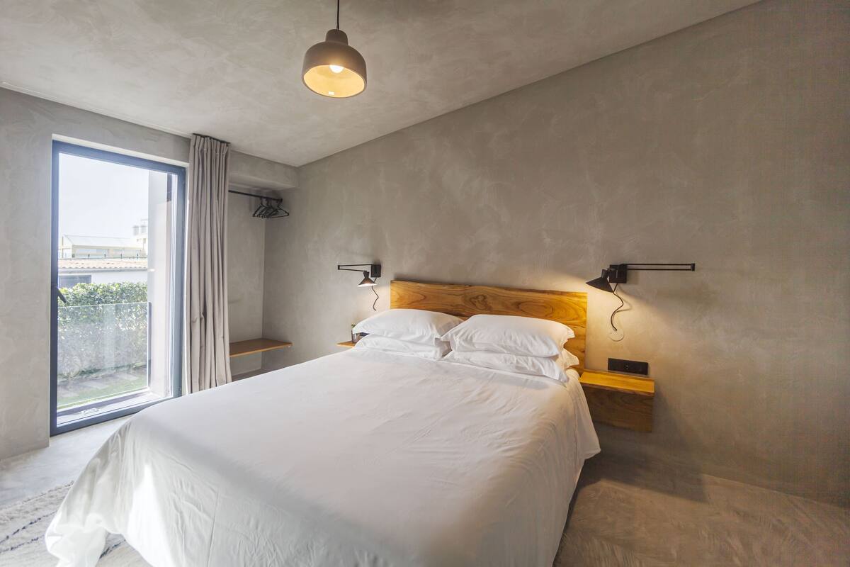 A modern bedroom with a large bed, a wooden headboard, bedside tables, and a hanging light fixture.