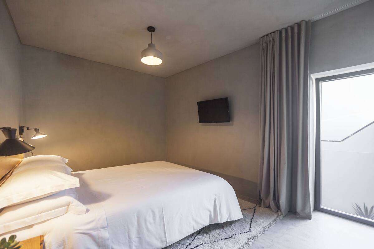 A modern bedroom with a large bed, a flat-screen TV, and a large window with curtains.
