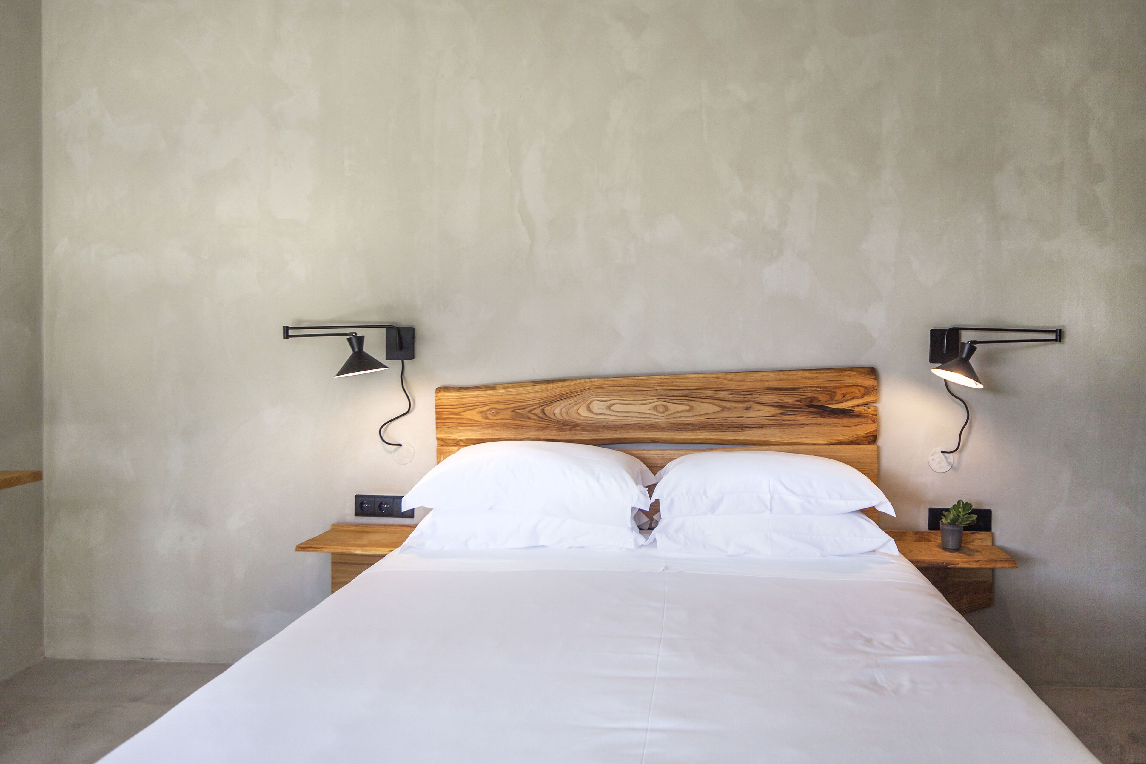 A bedroom with a wooden headboard, white bedding, two bedside tables with lamps, and a small plant on one table.