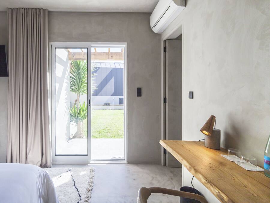 Una habitación de hotel moderna con una cama, un escritorio de madera, una botella y vistas al exterior a través de una puerta corrediza.