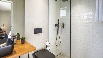A bathroom with a shower, toilet, and a sink area with a mirror and a small shelf with plants.