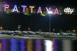 A nighttime view of Pattaya city with illuminated signs spelling out "PATTAYA city" and a marina with boats docked. - Chitra Villa (Pattaya)