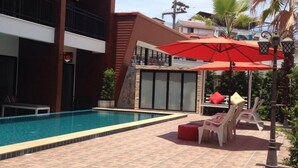 A swimming pool with tiled flooring, surrounded by lounge chairs and a red umbrella. - Chitra Villa (Pattaya)