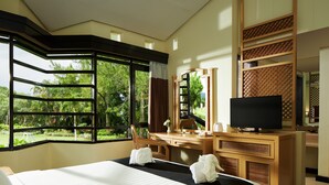 Een hotelkamer met een groot bed, een bureau met een televisie, en uitzicht op groen buiten het raam.