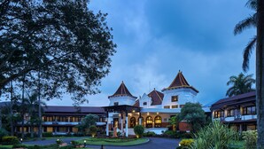 Een groot, meerhoog hotel met een centrale binnenplaats, omgeven door weelderige tuinen en palmbomen.