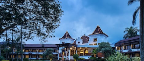 A large, multi-story hotel with a central courtyard, surrounded by lush gardens and palm trees.