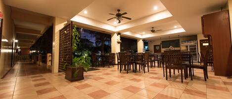 A spacious indoor area with a checkered floor, multiple tables and chairs, ceiling fans, and a large potted plant.