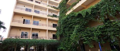 A multi-story building with a swimming pool, outdoor seating, and greenery.