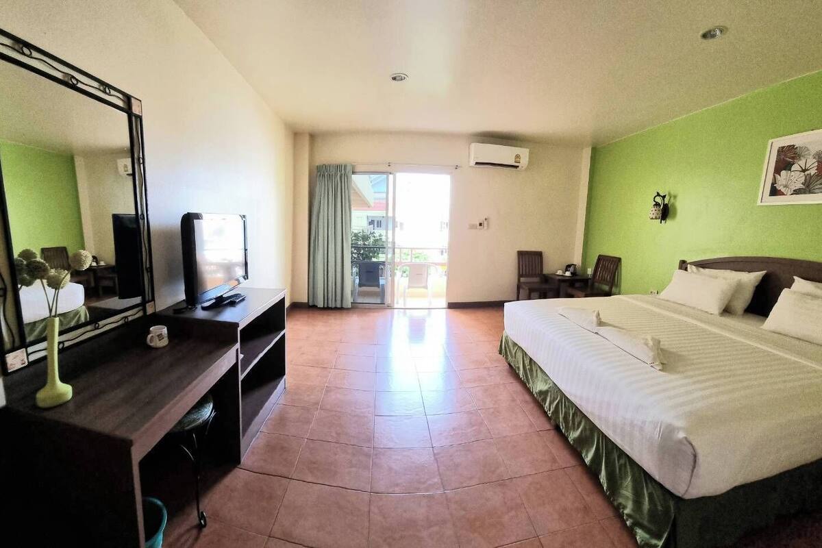 A hotel room with a bed, a desk with a TV, a mirror, and a green wall.