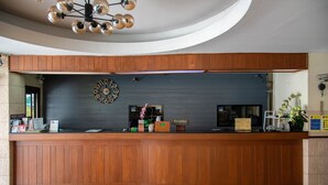 A reception desk with a clock, a reception sign, and a potted plant. - Opey De Place (Pattaya)
