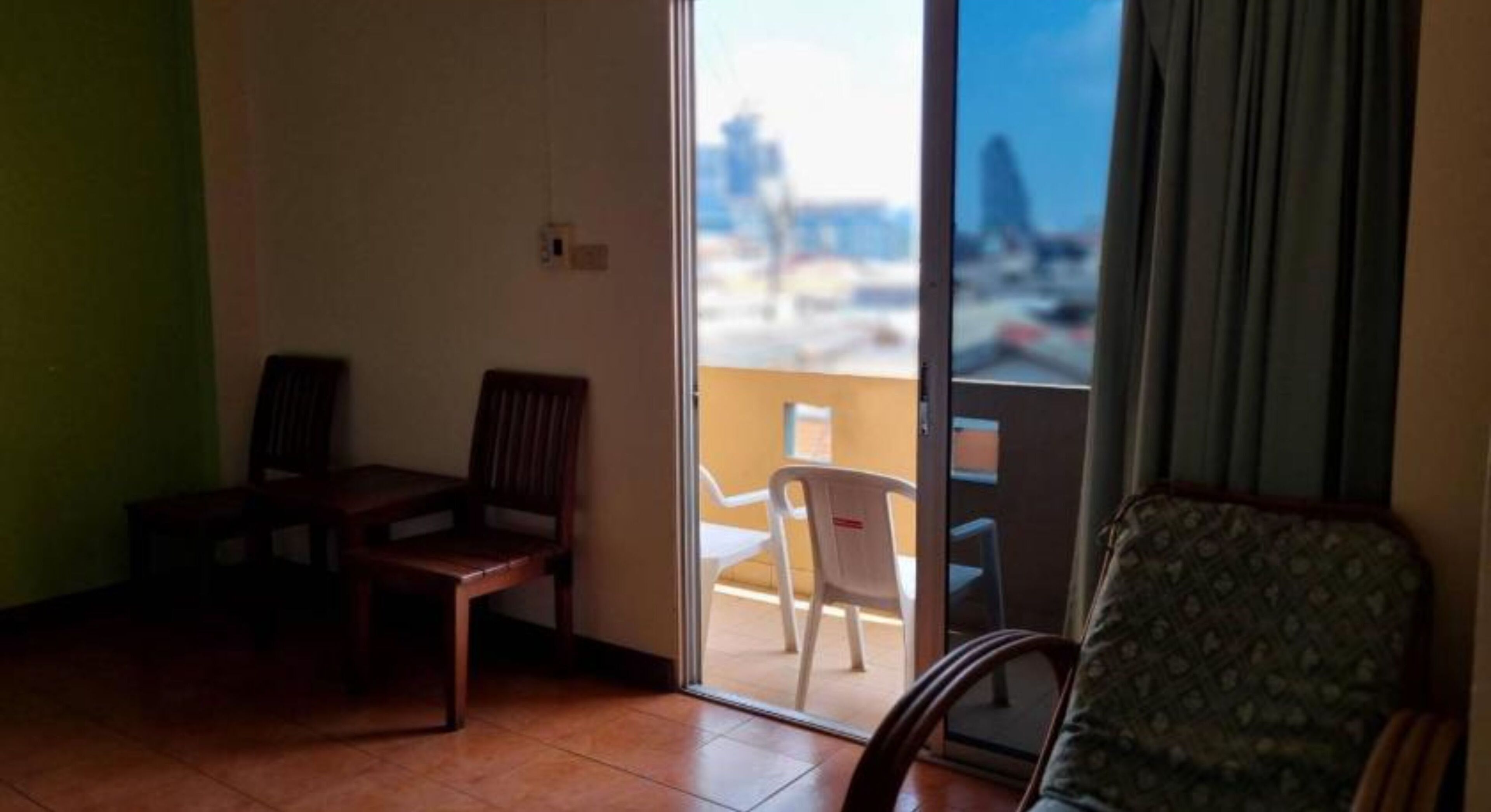 Um quarto com duas cadeiras de madeira, um sofá estampado e uma porta de vidro deslizante para uma área externa com uma cadeira branca.