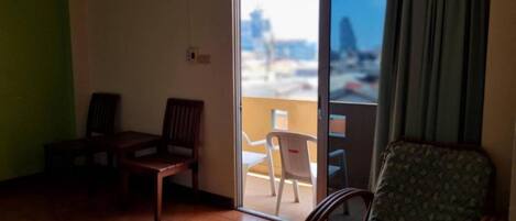 Um quarto com duas cadeiras de madeira, um sofá estampado e uma porta de vidro deslizante para uma área externa com uma cadeira branca.