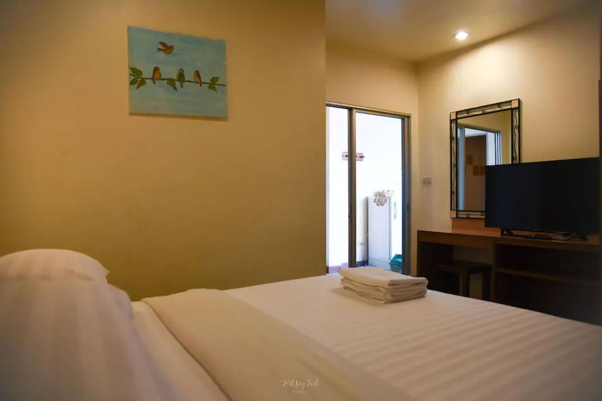 A hotel room with a bed, a painting of birds on the wall, a television, and a mirror.