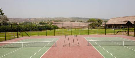 An outdoor tennis court with two courts, surrounded by a fence, and a building in the background.