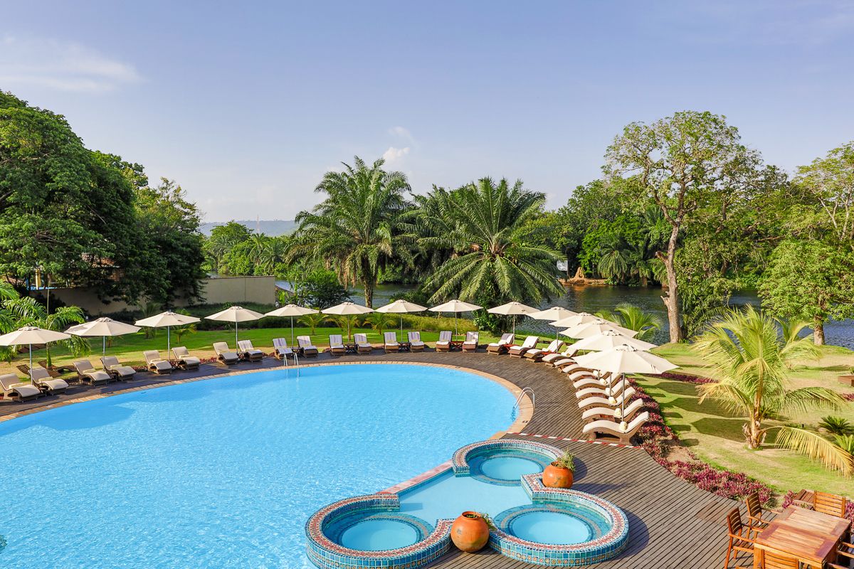 A large, curved swimming pool with lounge chairs and umbrellas, surrounded by lush greenery and palm trees.