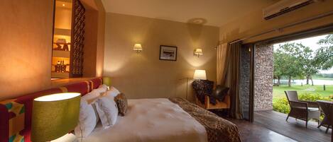 A hotel room with a large bed, two bedside lamps, a window with a view of a garden, and an air conditioning unit.