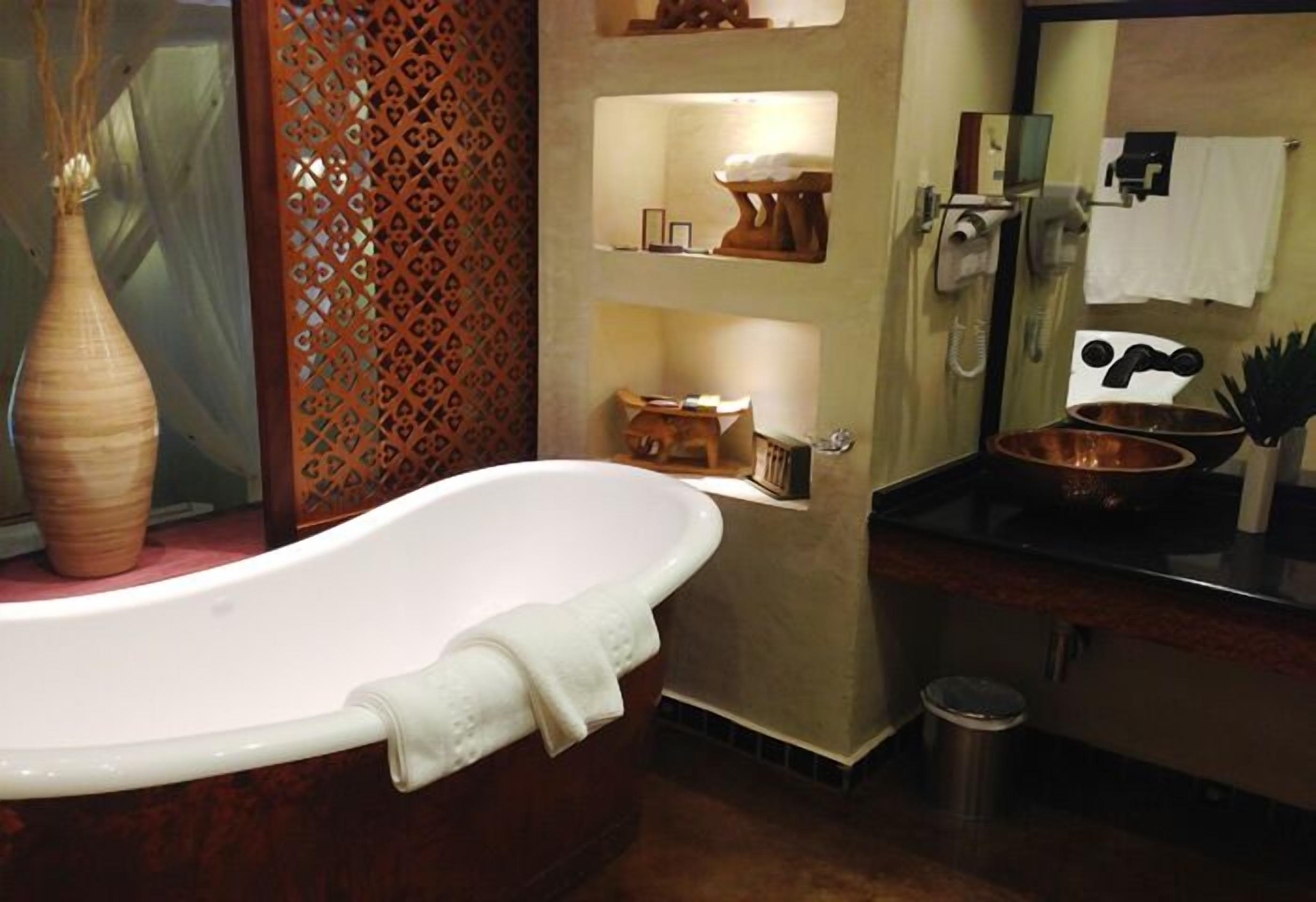 A bathroom with a freestanding bathtub, a wooden vanity with a copper basin, and a decorative wooden panel with cut-out patterns.