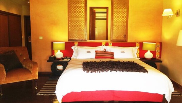 A hotel room with a large bed, two bedside tables, a chair, and a mirror with decorative panels. - The Royal Senchi Hotel and Resort (Akosombo)