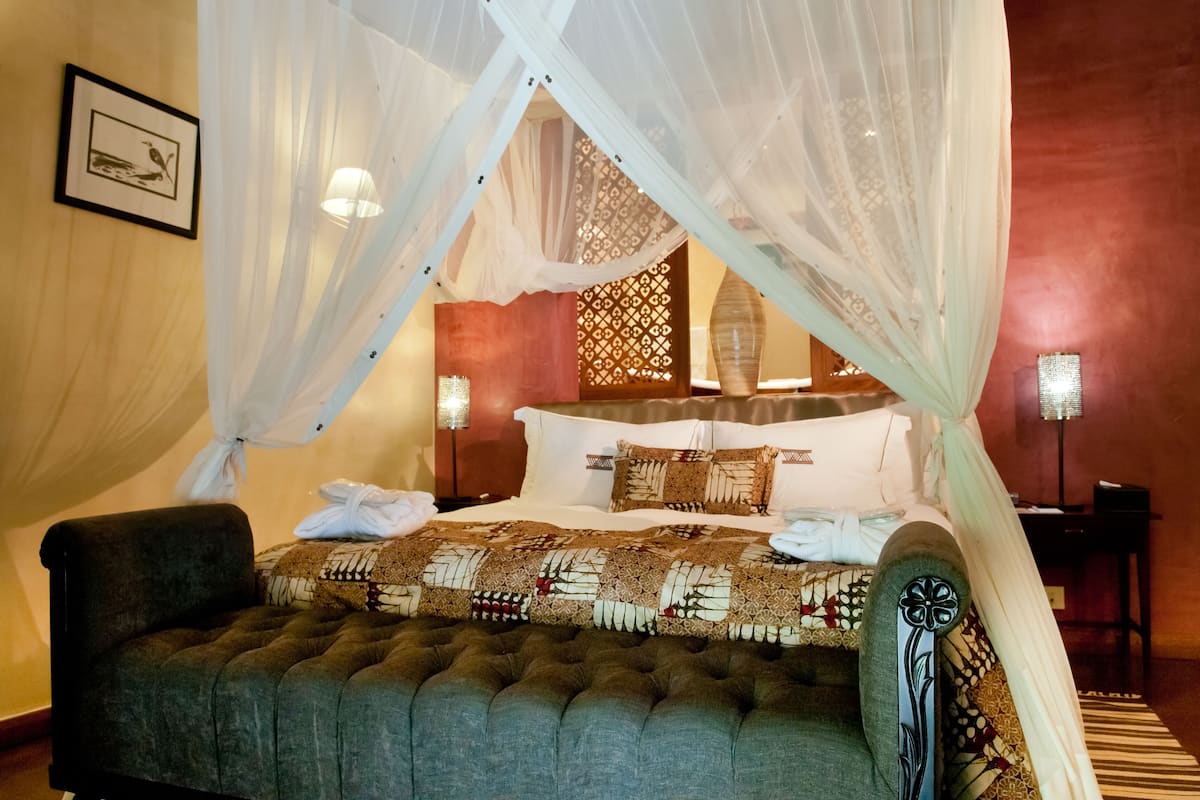 A bedroom with a four-poster bed, a tufted bench, and a nightstand with a lamp.