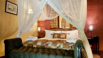 A bedroom with a four-poster bed, a tufted bench, and a nightstand with a lamp.