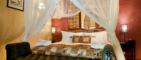 A bedroom with a four-poster bed, a tufted bench, and a nightstand with a lamp.