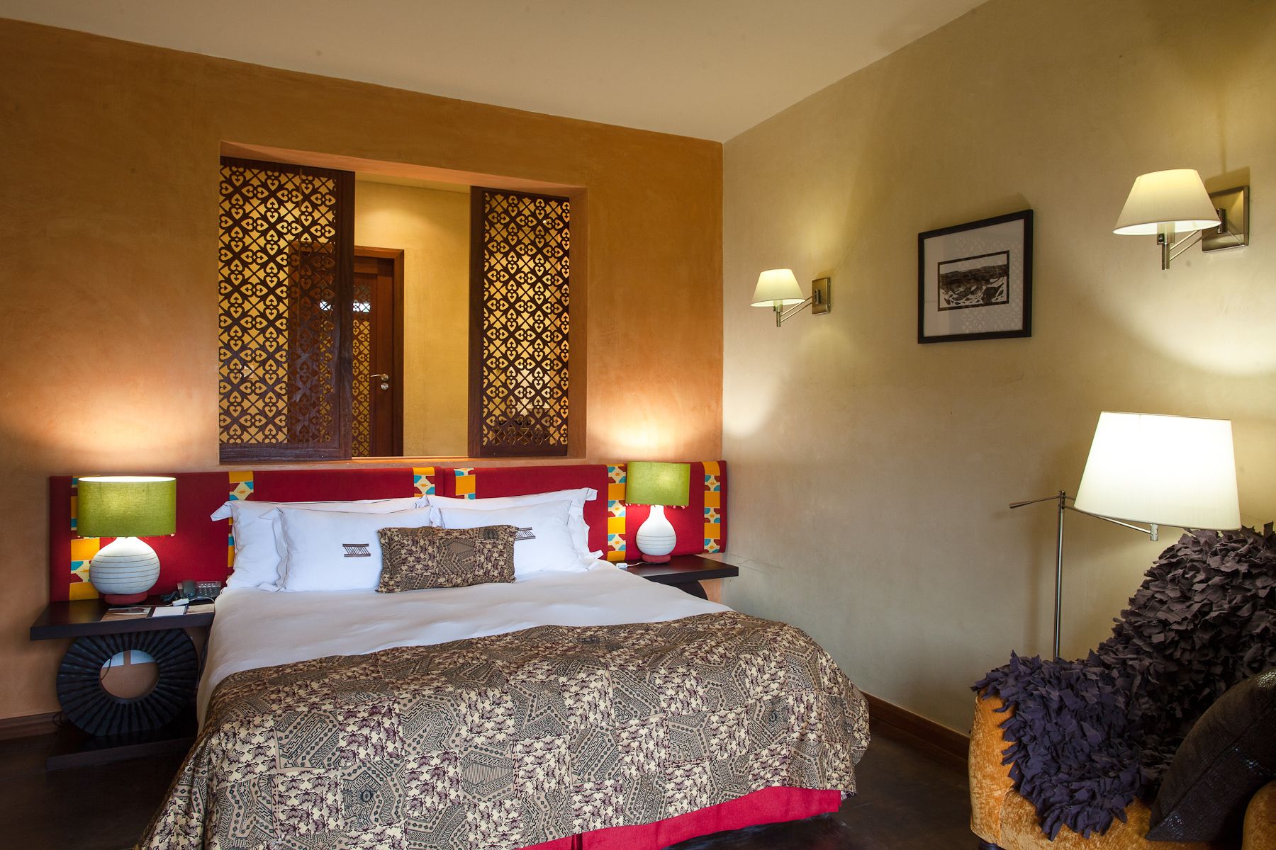 Une chambre d’hôtel avec un grand lit, deux lampes de chevet, une table de chevet, un panneau décoratif au mur et un tableau encadré accroché au mur.