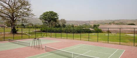 A tennis court with a net, surrounded by a fence, and a tree in the background.